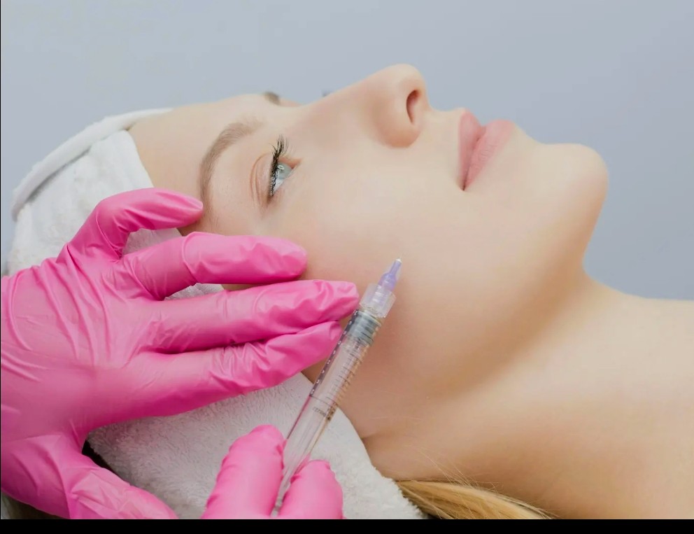 Suntikan skinbooster di pipi pasien wanita oleh tangan bersarung tangan medis merah muda